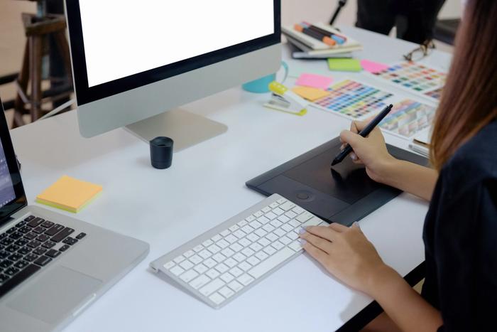 a woman is sitting at a desk using a graphic tablet and a computer .