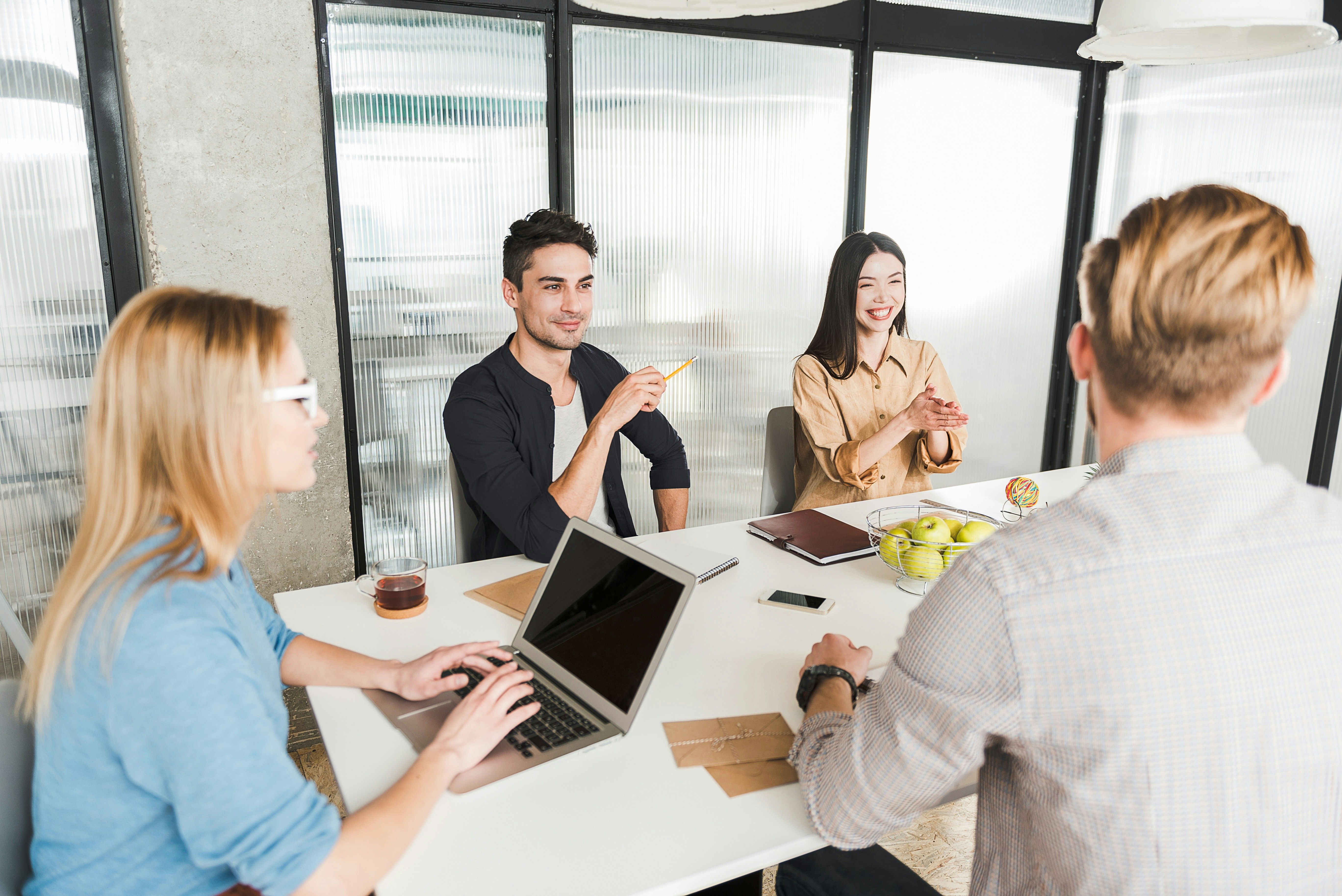 a group of people are sitting around a table with laptops .