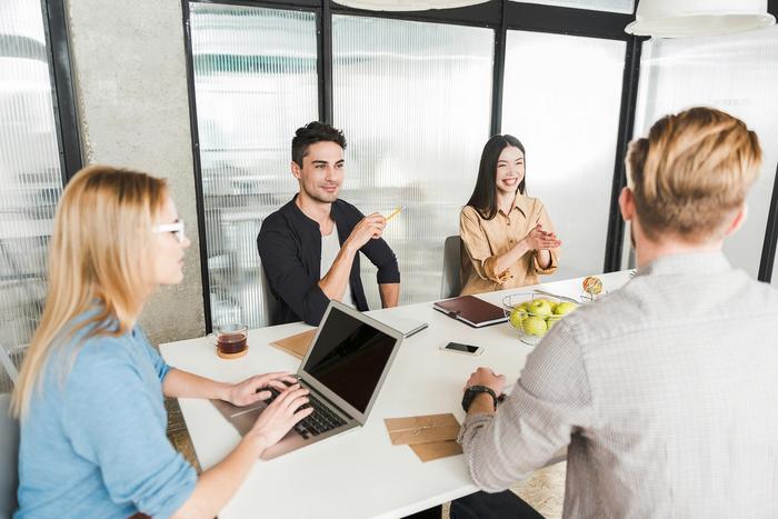a group of people are sitting around a table with laptops .