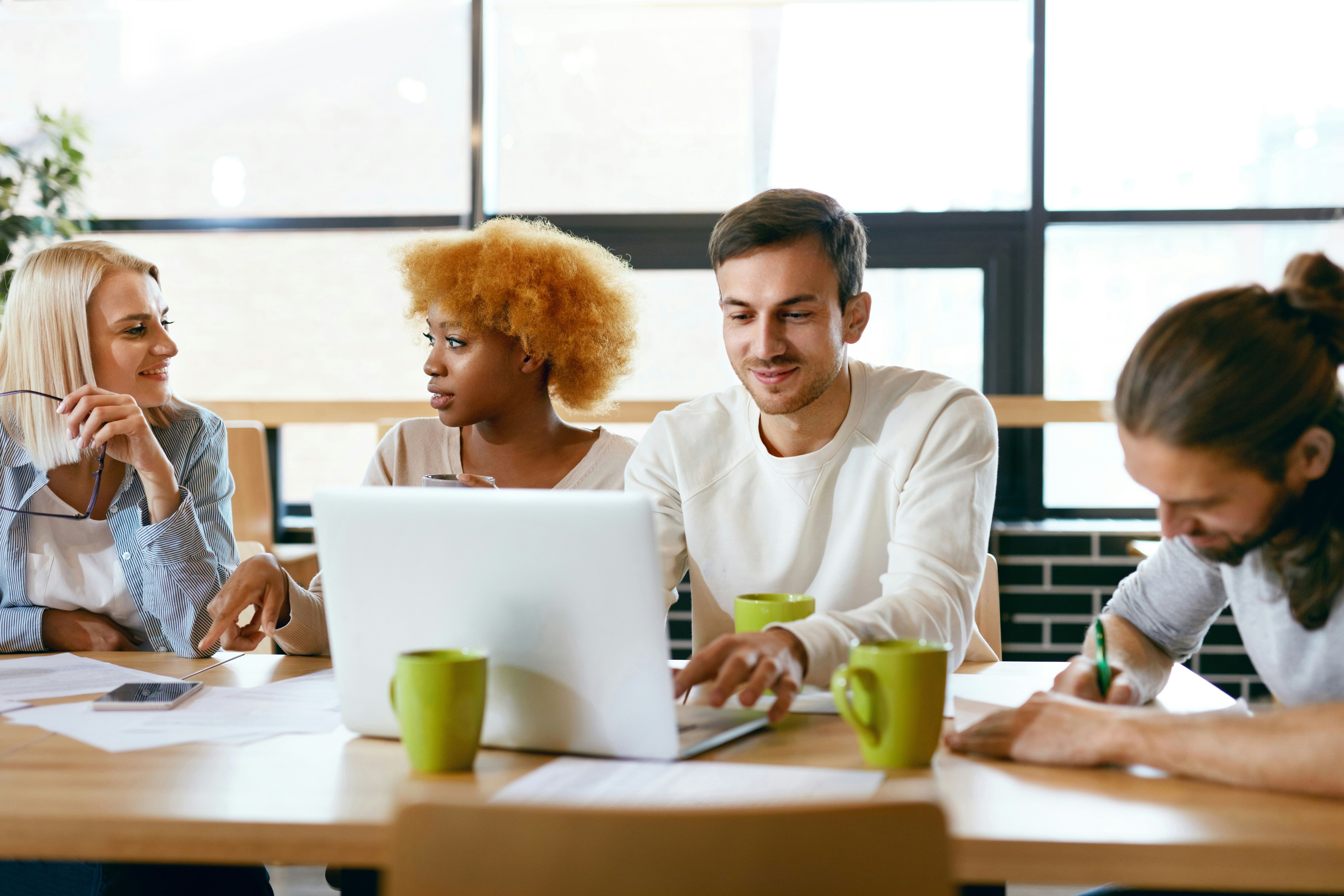 a group of people are sitting at a table looking at a laptop computer .