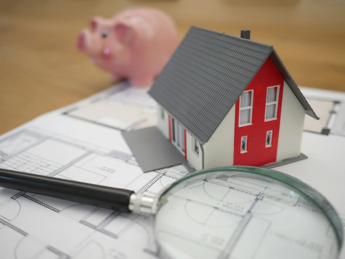 A piggy bank, and a model house on top of some blueprints next to a magnifying glass