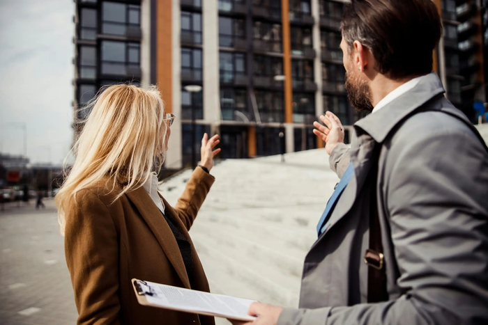 2 people with a clipboard pointing at a building