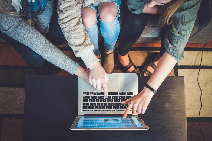 Three people sat around a laptop pointing at the screen