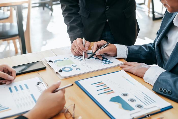 a group of business people are sitting at a table looking at charts and graphs .