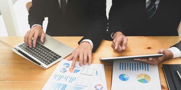 a group of business people are sitting at a table looking at charts and graphs .