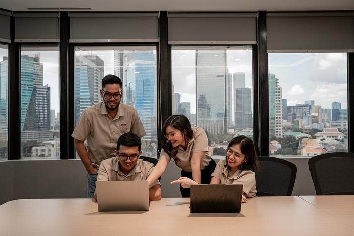 Four colleagues collaborating on laptops in an office with a city skyline.