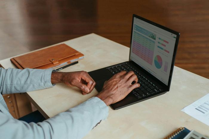 a man is typing on a laptop computer at a desk .