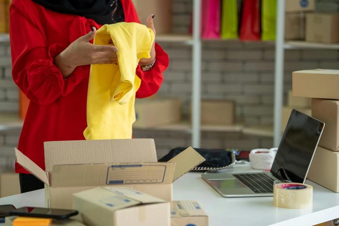 a woman is putting a yellow shirt in a cardboard box .
