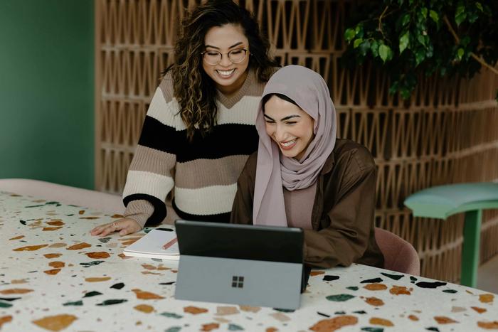 two women are sitting at a table looking at a laptop computer .