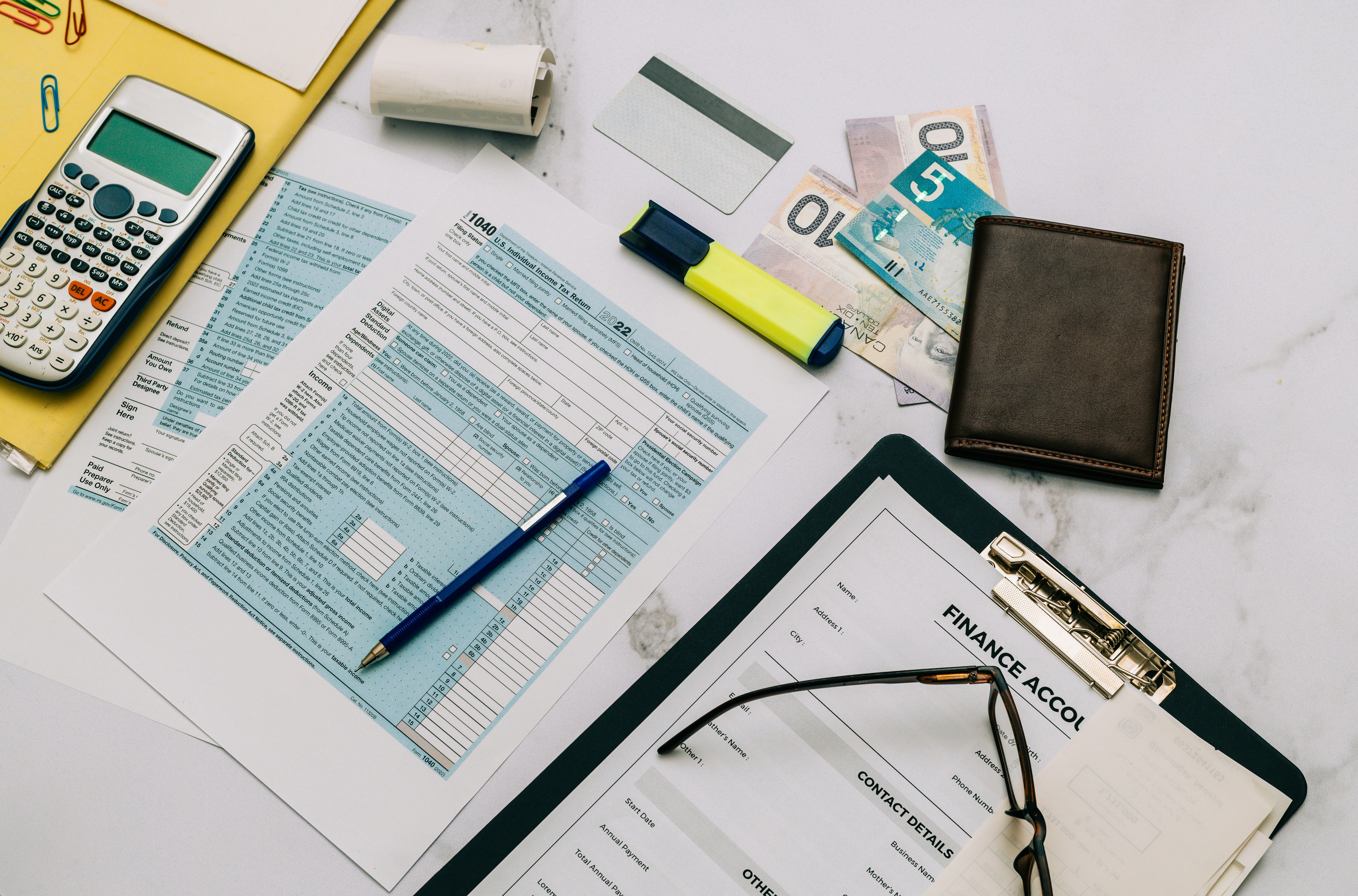 a clipboard with a pen , calculator , credit card , and money on it .
