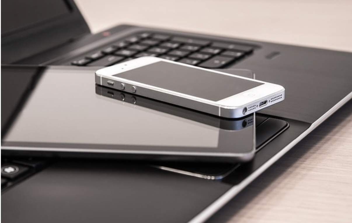 a cell phone laying on top of a tablet next to a laptop