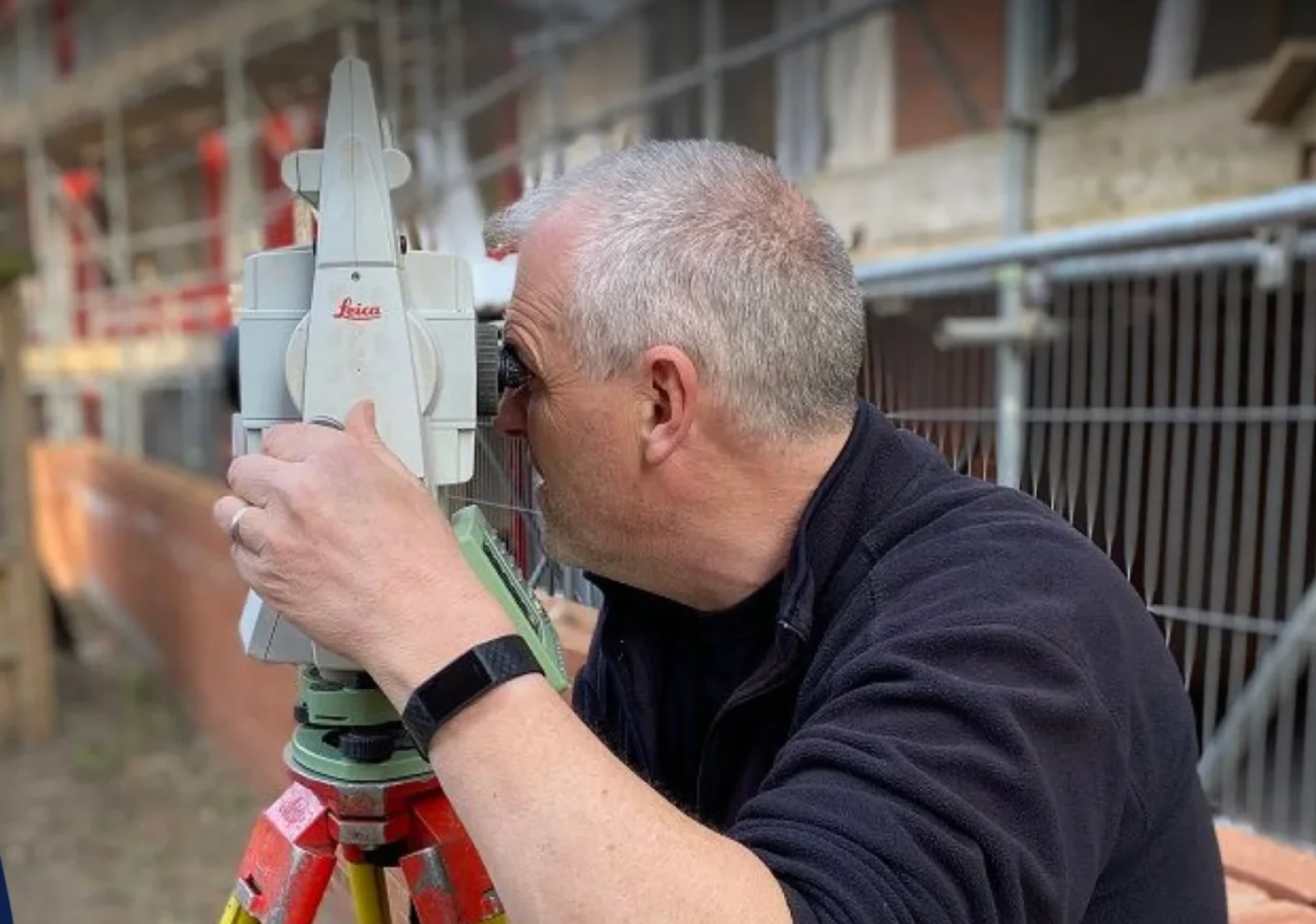 A man looking through a Leica surveying instrument at a construction site.