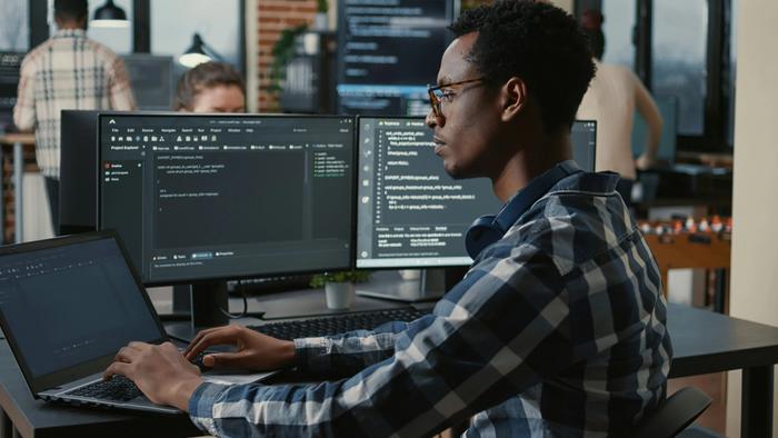 a man is sitting at a desk using a laptop and a computer .