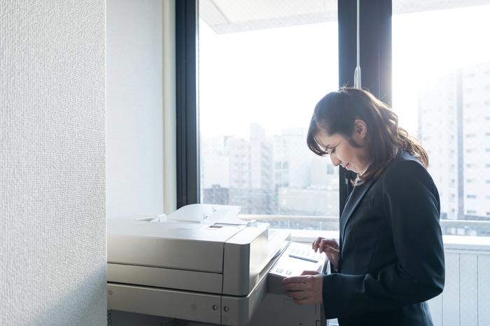 a woman in a suit is using a printer in an office .