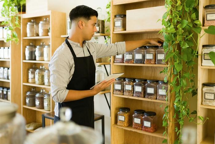 a man is looking at a tablet while standing in front of a shelf full of jars .