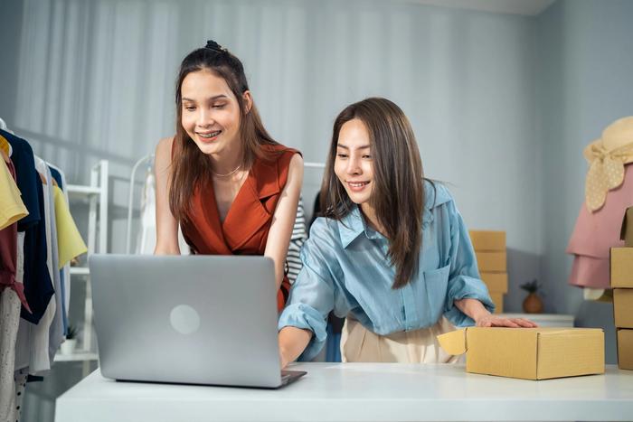 two women are sitting at a table looking at a laptop computer .