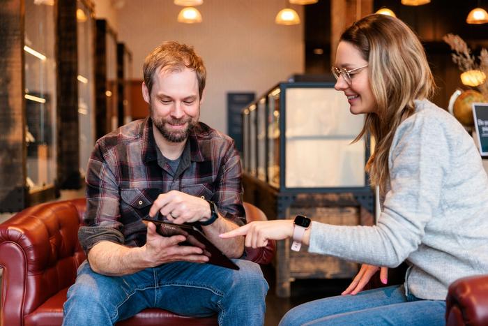 a man and a woman are sitting on a couch looking at a tablet .