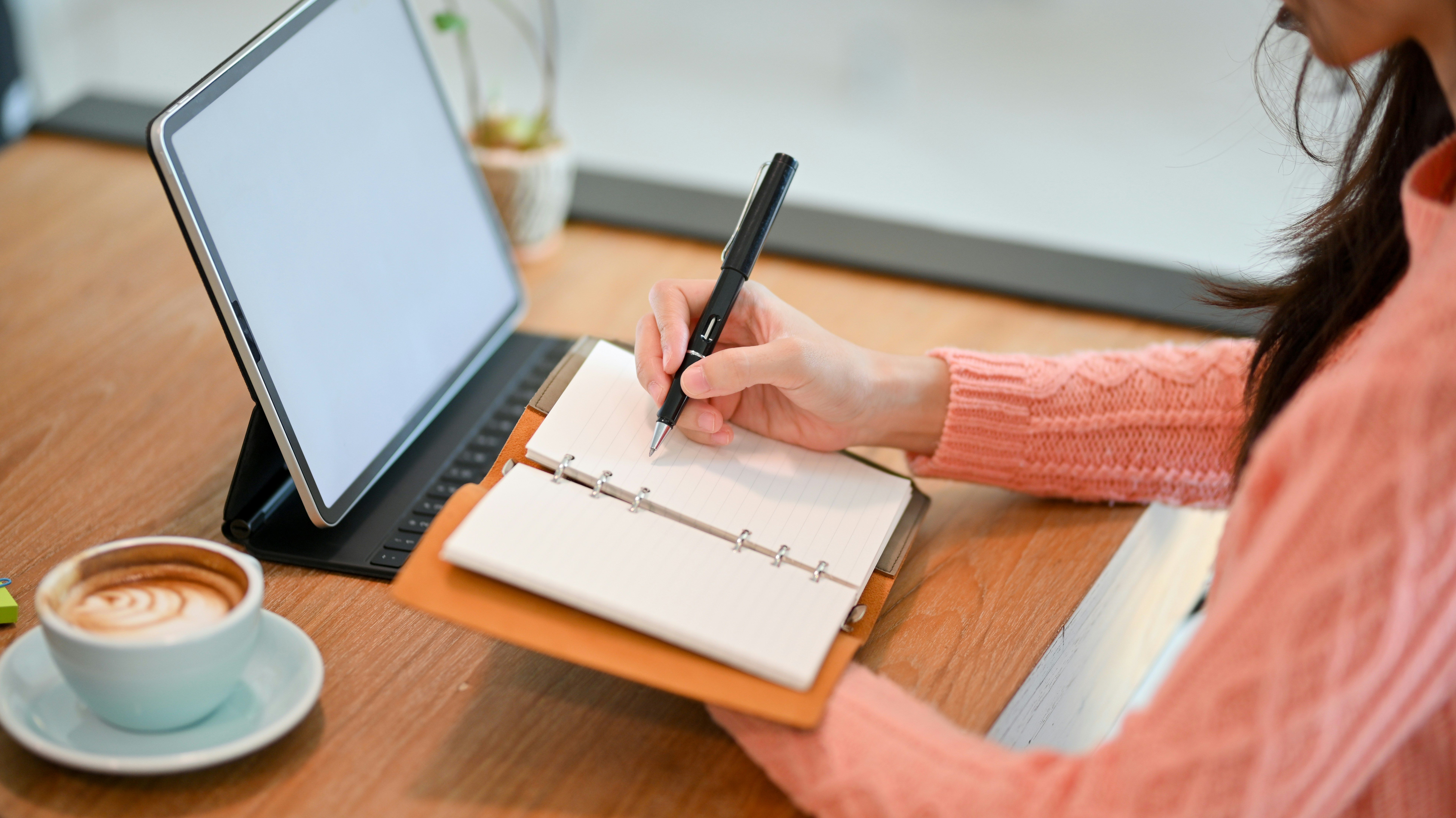 a woman is sitting at a table writing in a notebook .