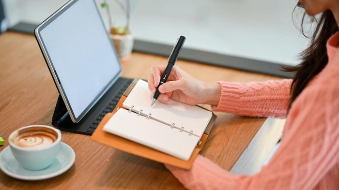 a woman is sitting at a table writing in a notebook .
