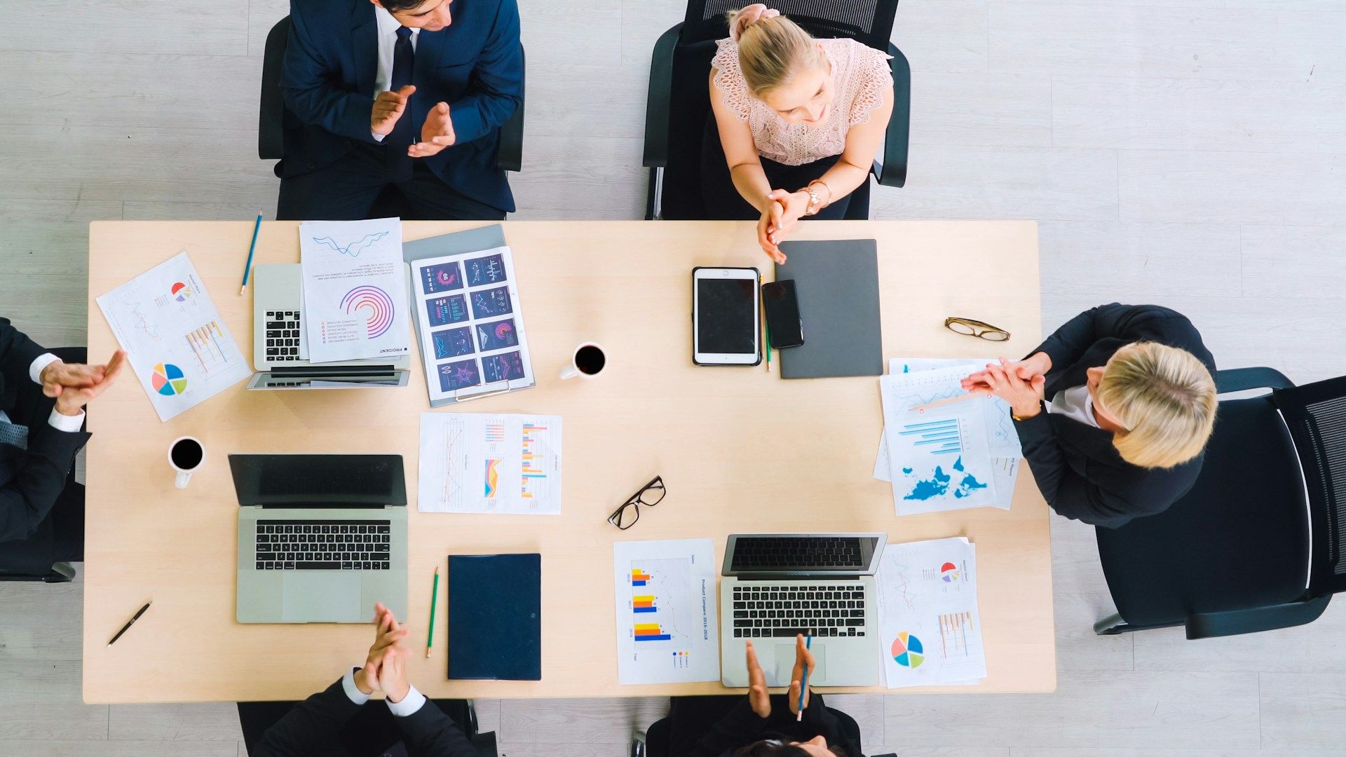 Office workers meet around a table with laptops and documents showing graphs, research and maps