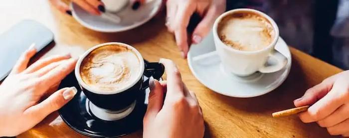 a group of people are sitting at a table drinking coffee .