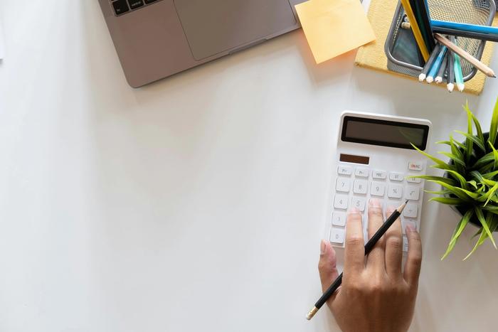 a person is using a calculator on a white desk .