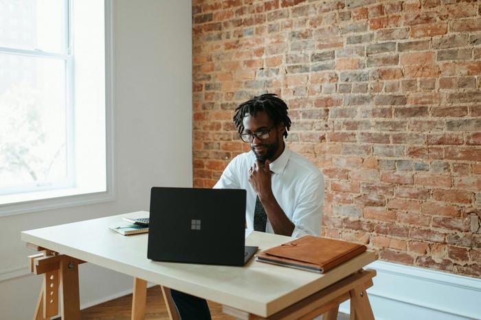 a man is sitting at a desk using a laptop computer.