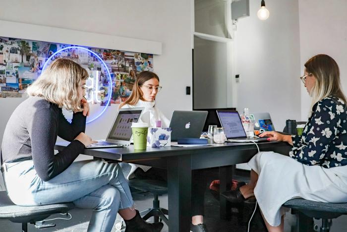 three women are sitting at a table with laptops .