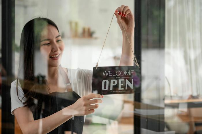 a woman is holding a welcome open sign in front of a glass door .