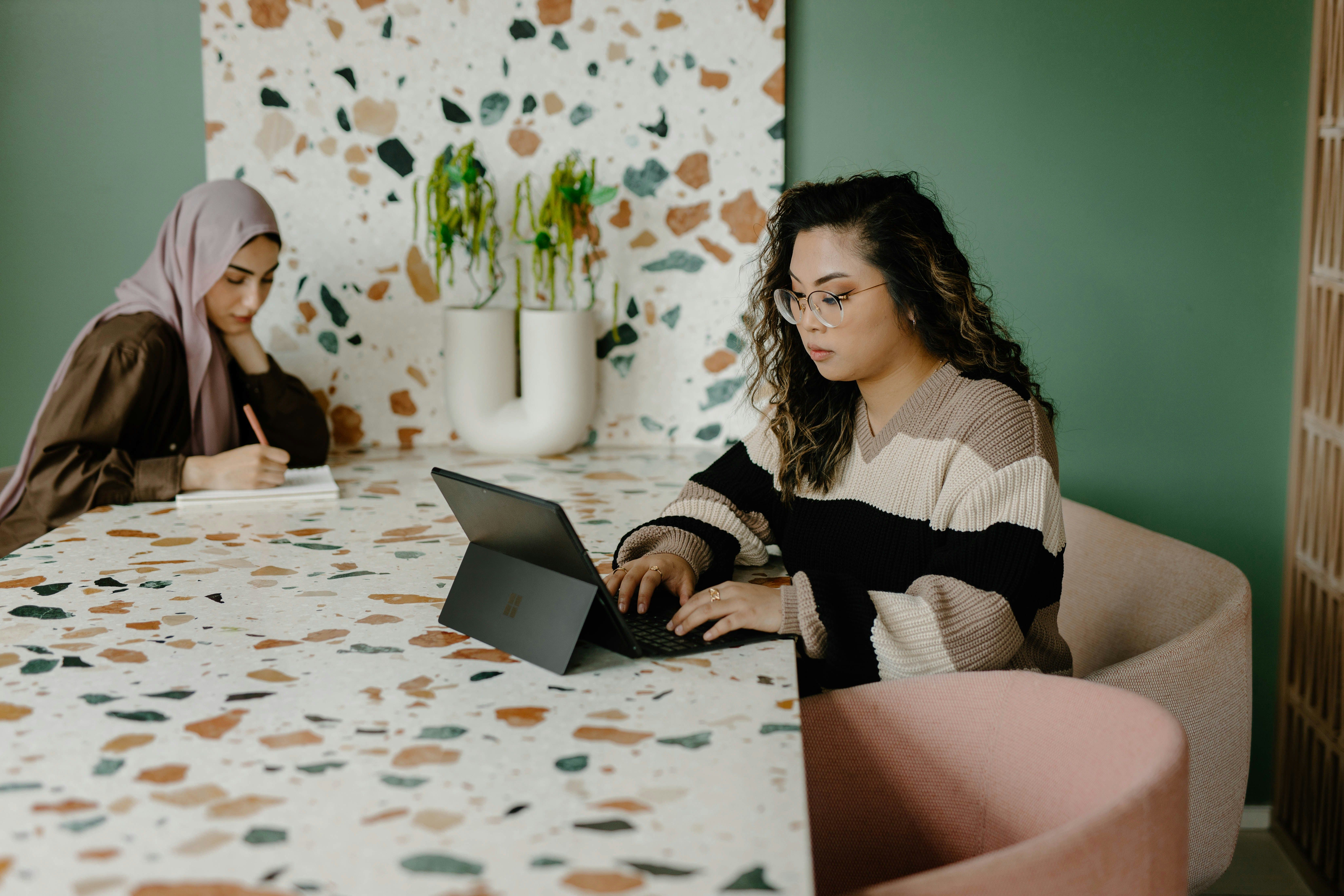 two women are sitting at a table using a tablet computer .