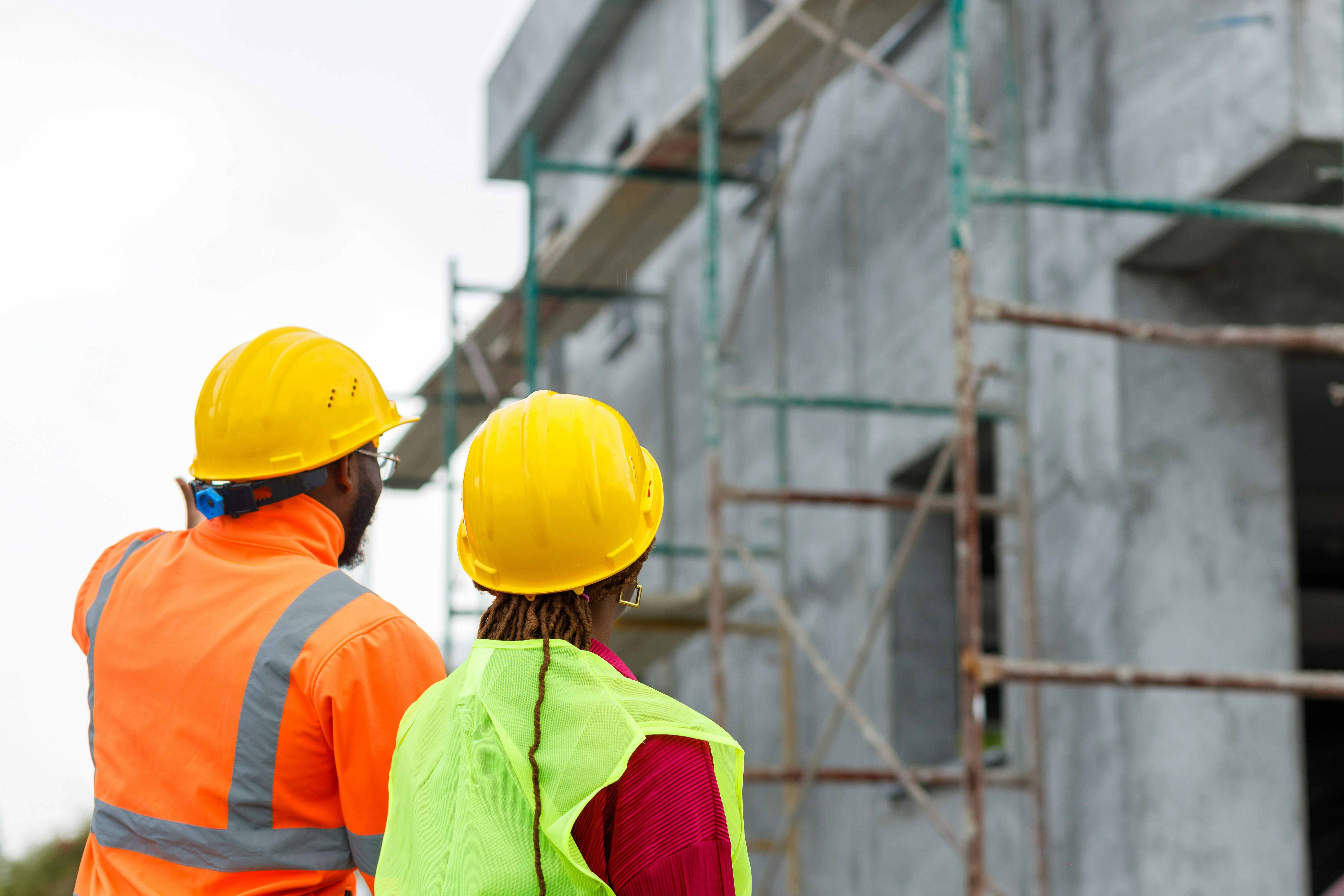 Two construction workers in hard hats observe a building under construction.