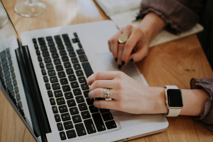 a woman is typing on a laptop computer while wearing an apple watch .