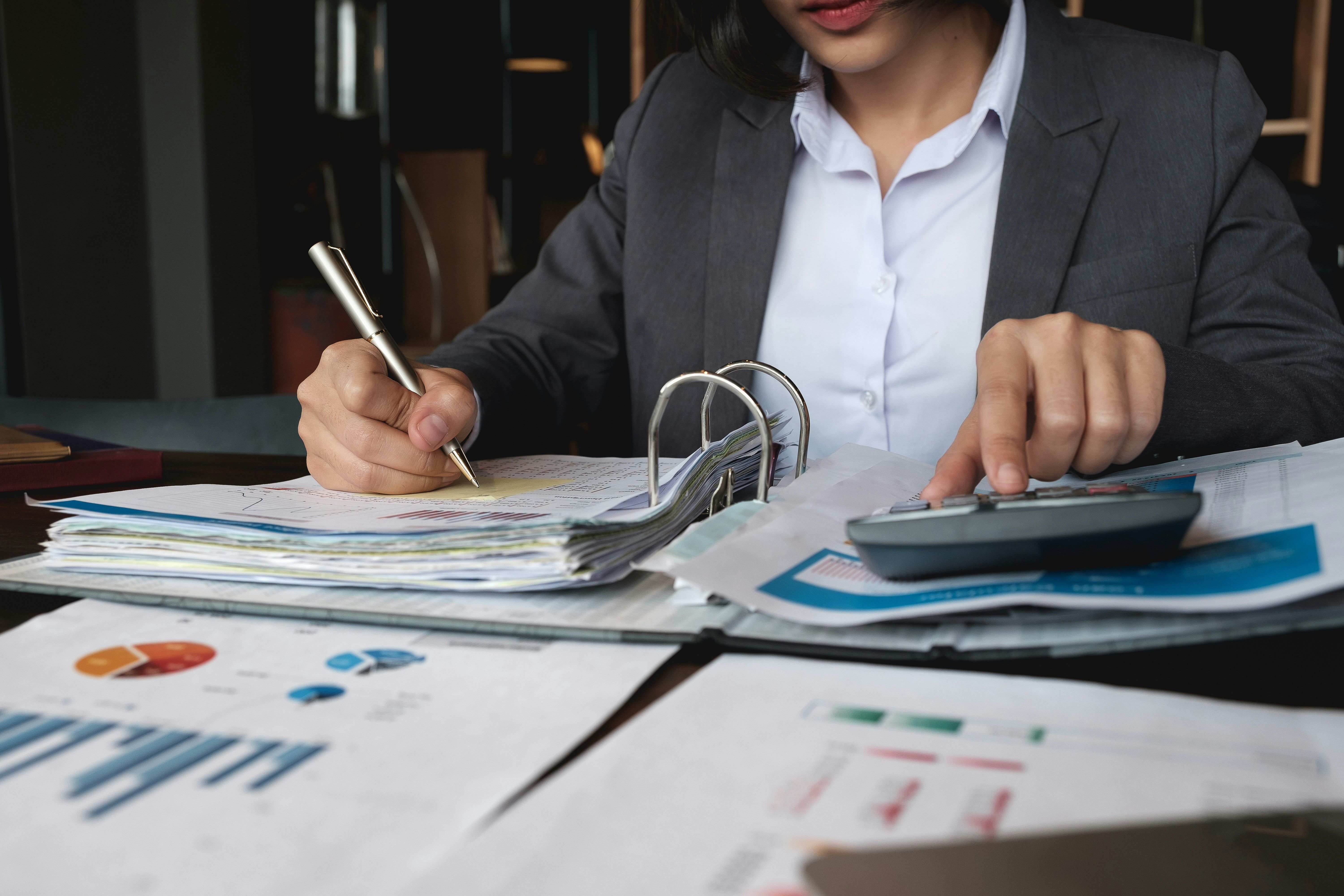 una mujer está usando una calculadora mientras revisa gráficos y hojas de cálculo