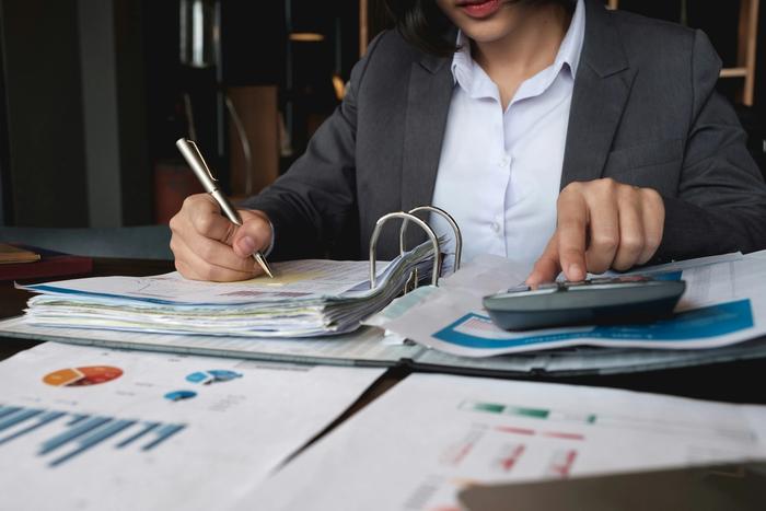 a woman is using a calculator while reviewing graphs and spreadsheets