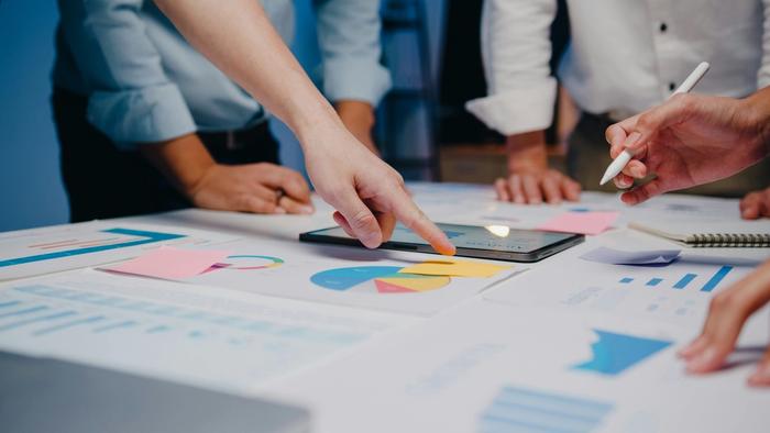 a group of people are sitting around a table looking at charts and graphs .