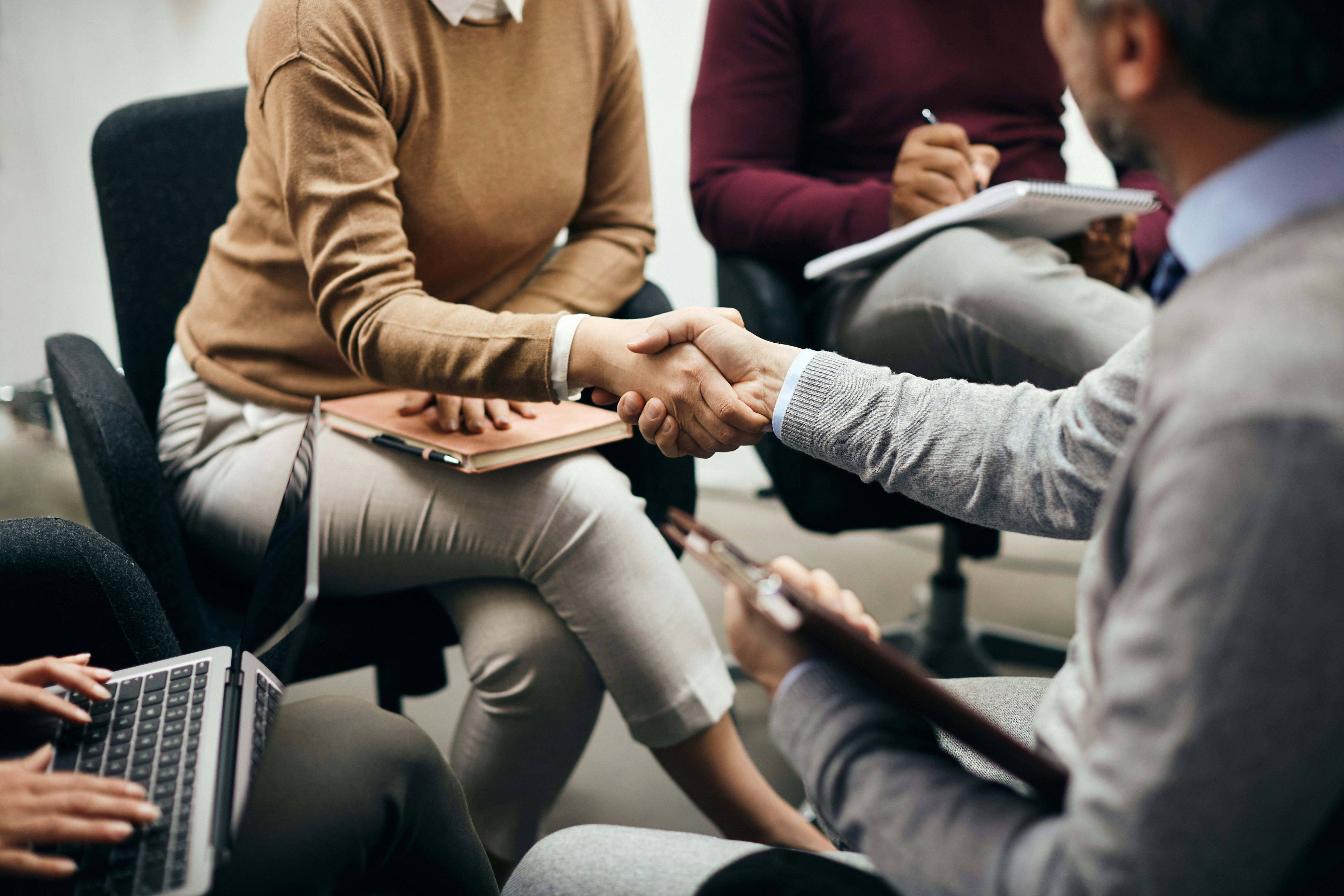 a group of people are sitting in chairs shaking hands .