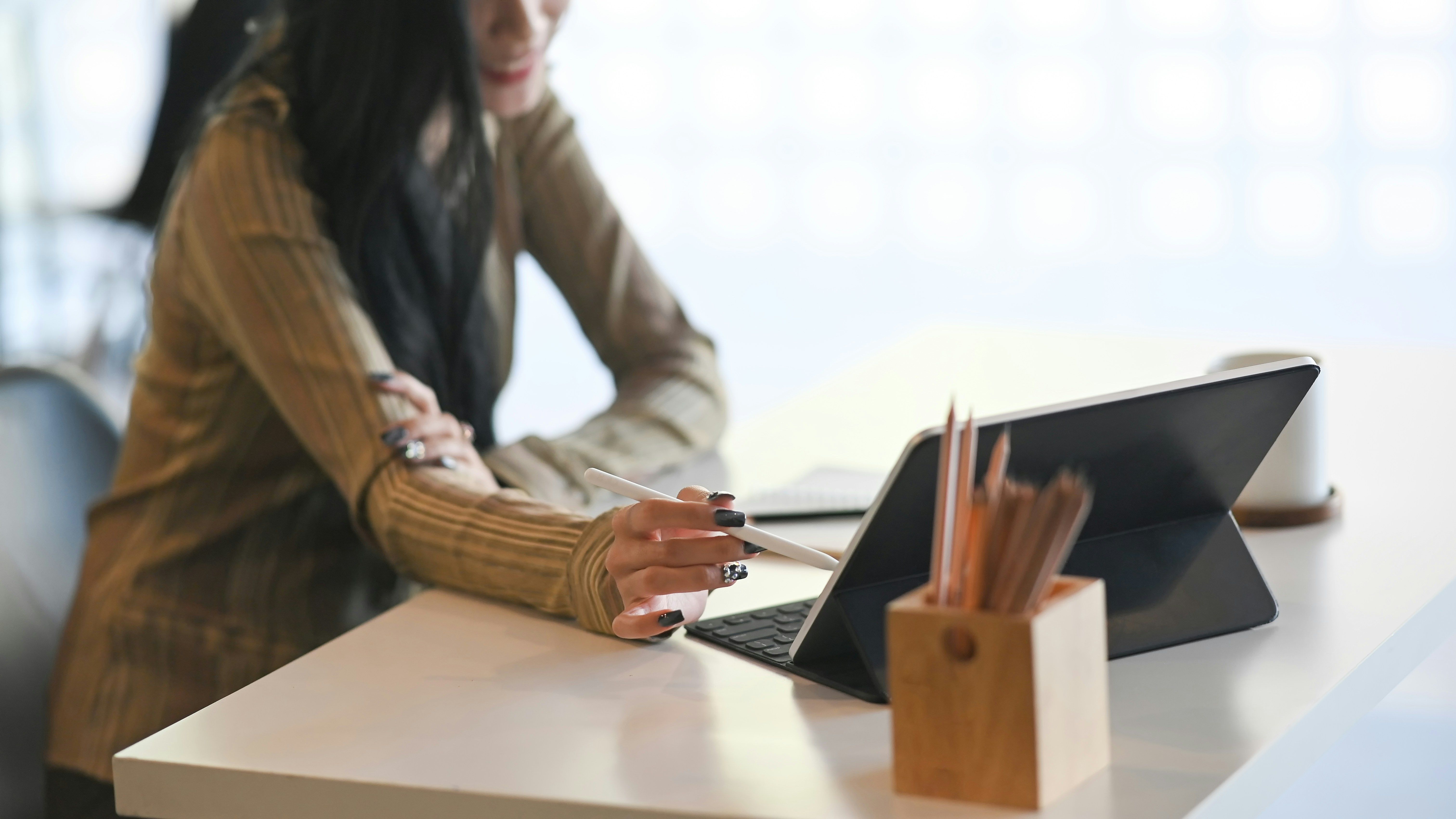 A woman uses a stylus on a tablet at a desk.