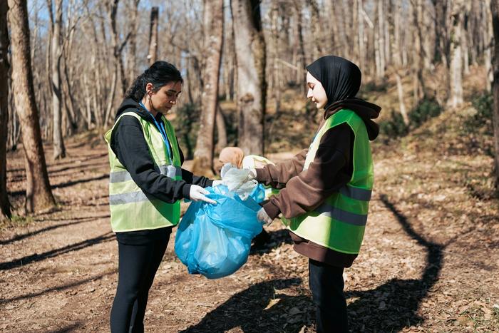 two young women are picking up trash in the woods .