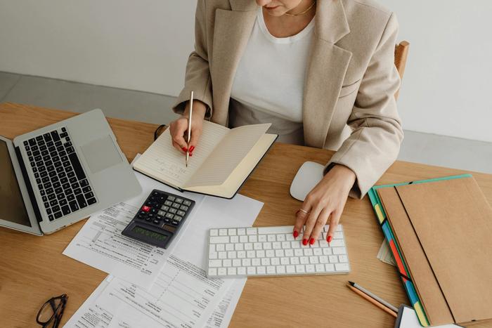 a woman is sitting at a desk with a calculator and a laptop .