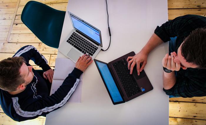 dois homens estão sentados à mesa usando laptops .