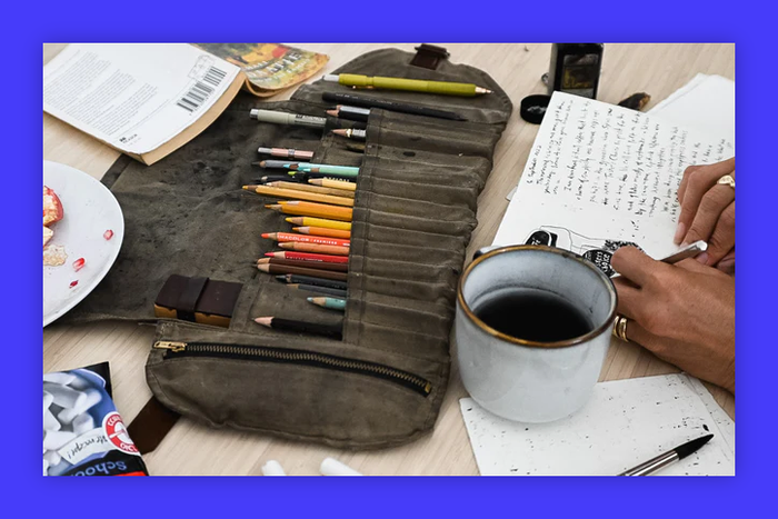 A roll of colored pencils sits on a table next to a cup of coffee.