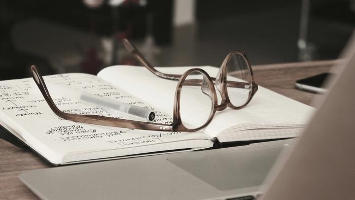 a pair of glasses is sitting on top of a notebook next to a laptop .