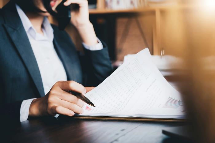 a woman is sitting at a desk talking on a cell phone while holding a pen and a piece of paper .