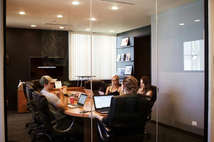 a group of people are sitting around a table in a conference room with laptops .