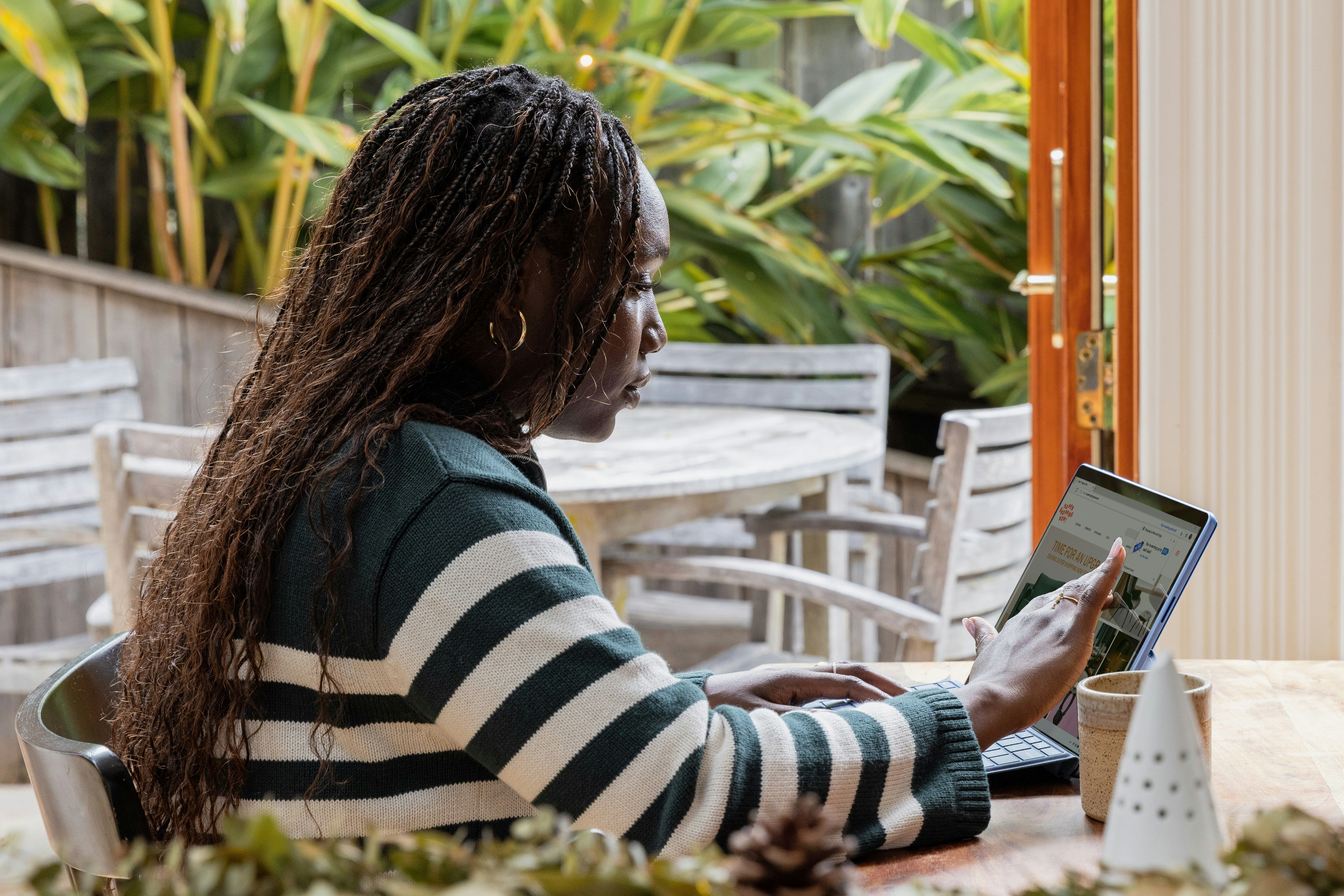 Person sitting at a table and using a tablet near an open window with plants outside.