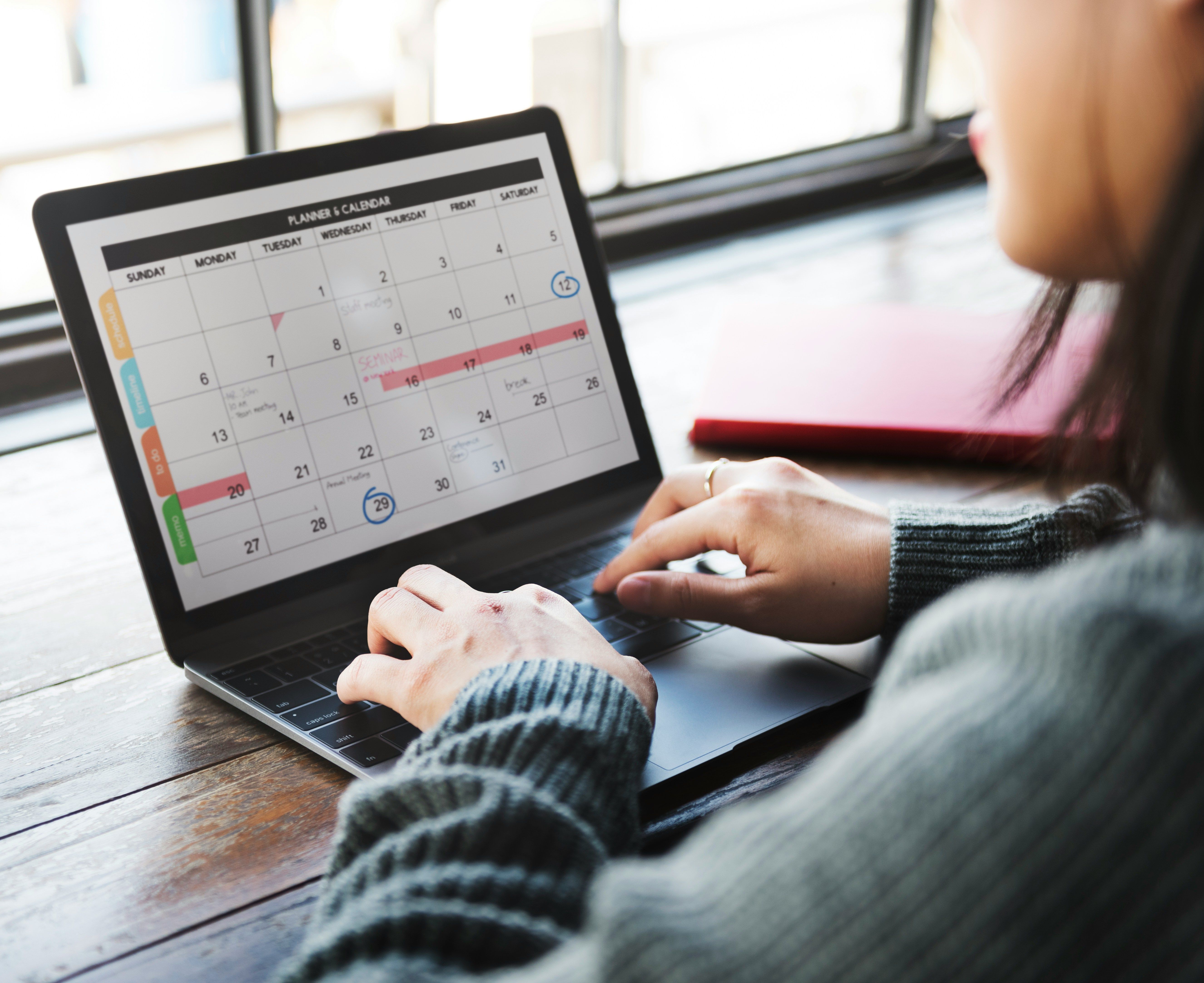 una mujer está escribiendo en una computadora portátil mientras mira un calendario .
