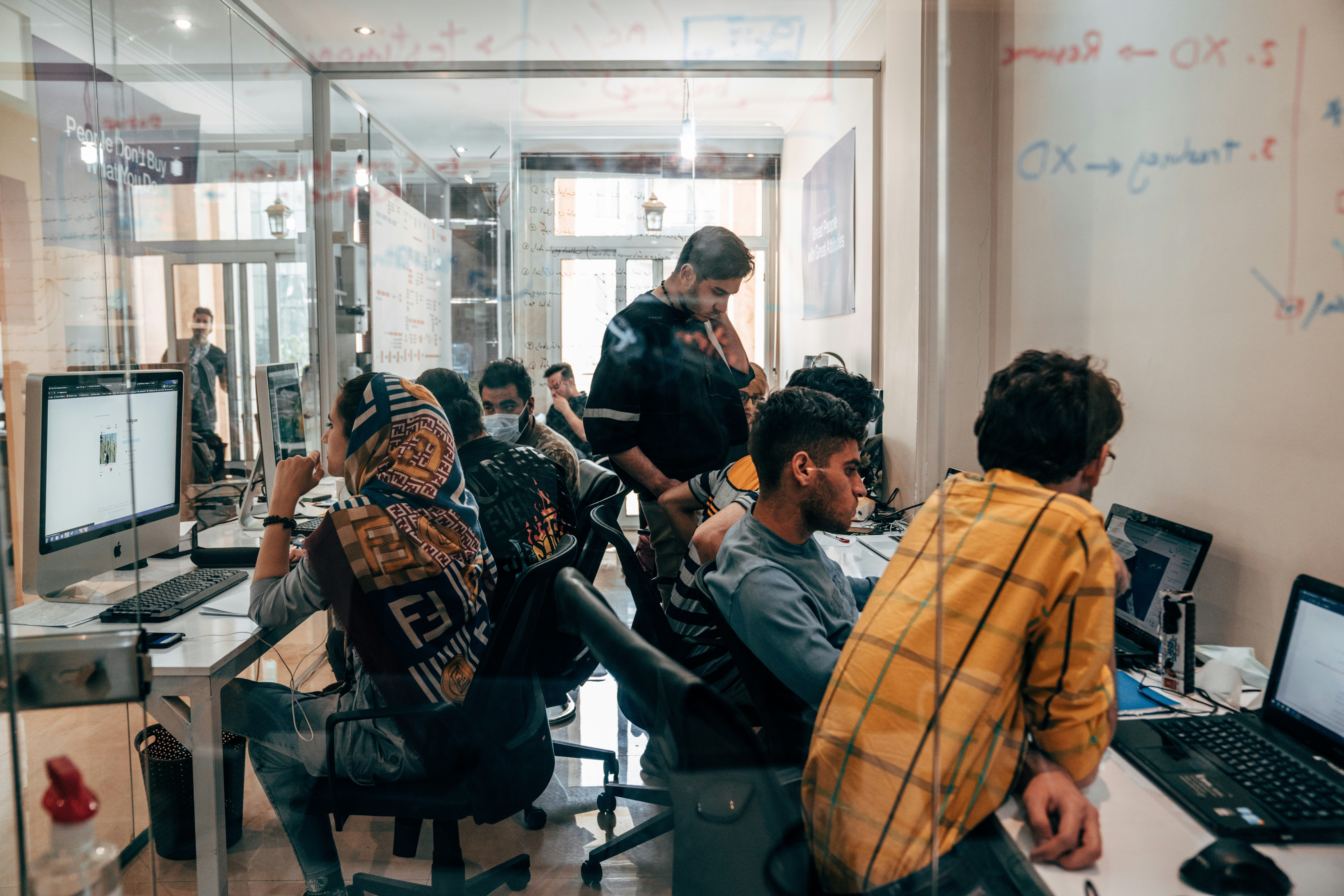 a group of people are sitting at desks in an office working on computers .