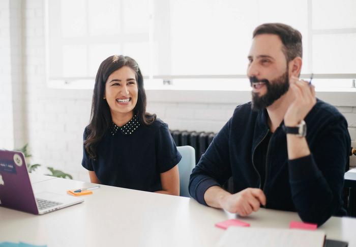 a man and a woman are sitting at a table with a laptop .