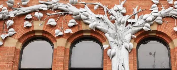 there is a sculpture of a tree on the side of a building .