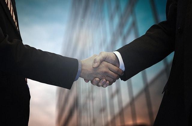 Two men in suits shaking hands in front of a building.